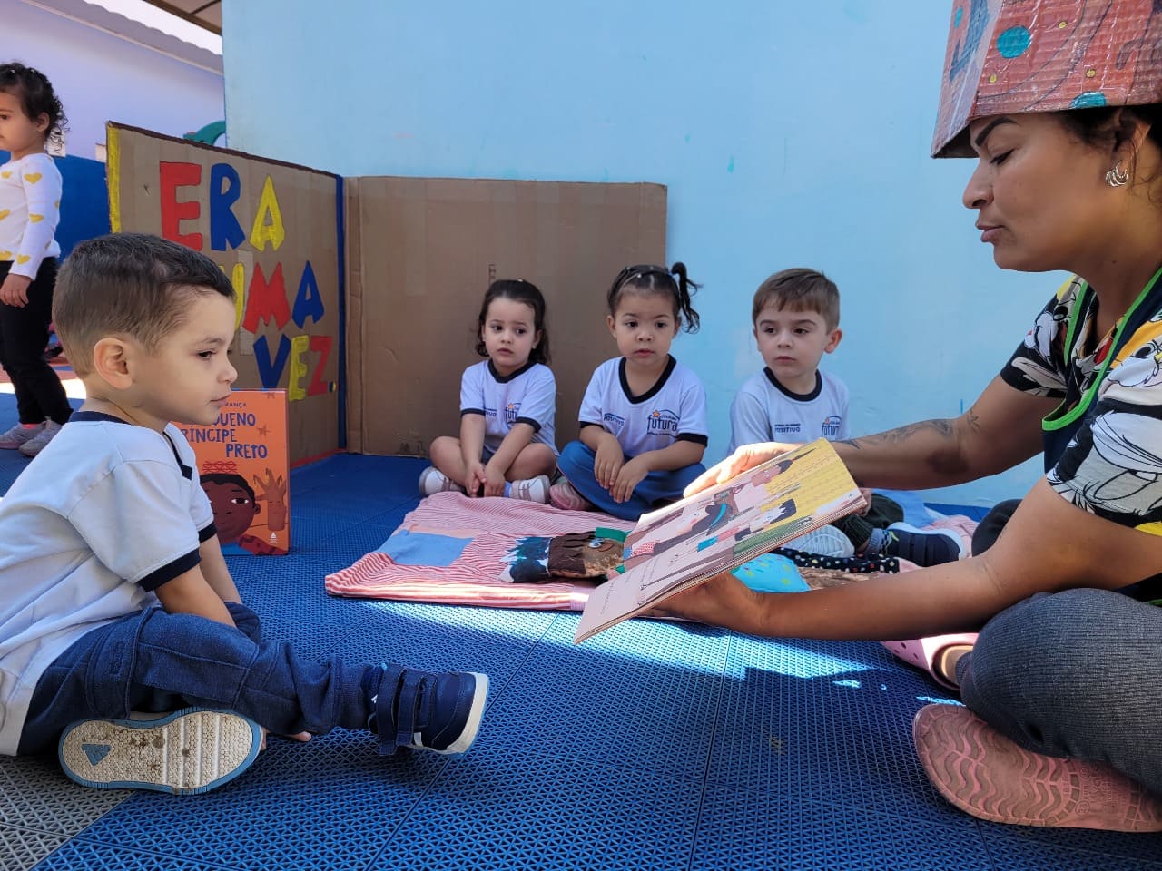 Professora do Colégio Futura Infantil lendo história para crianças durante o Projeto Ler é Descobrir Tesouros.
