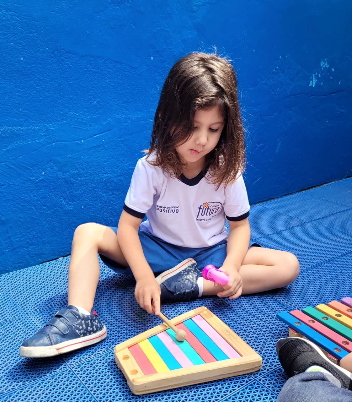 Menina concentrada tocando um xilofone em aula do projeto de música no Colégio Futura Infantil Jundiaí.