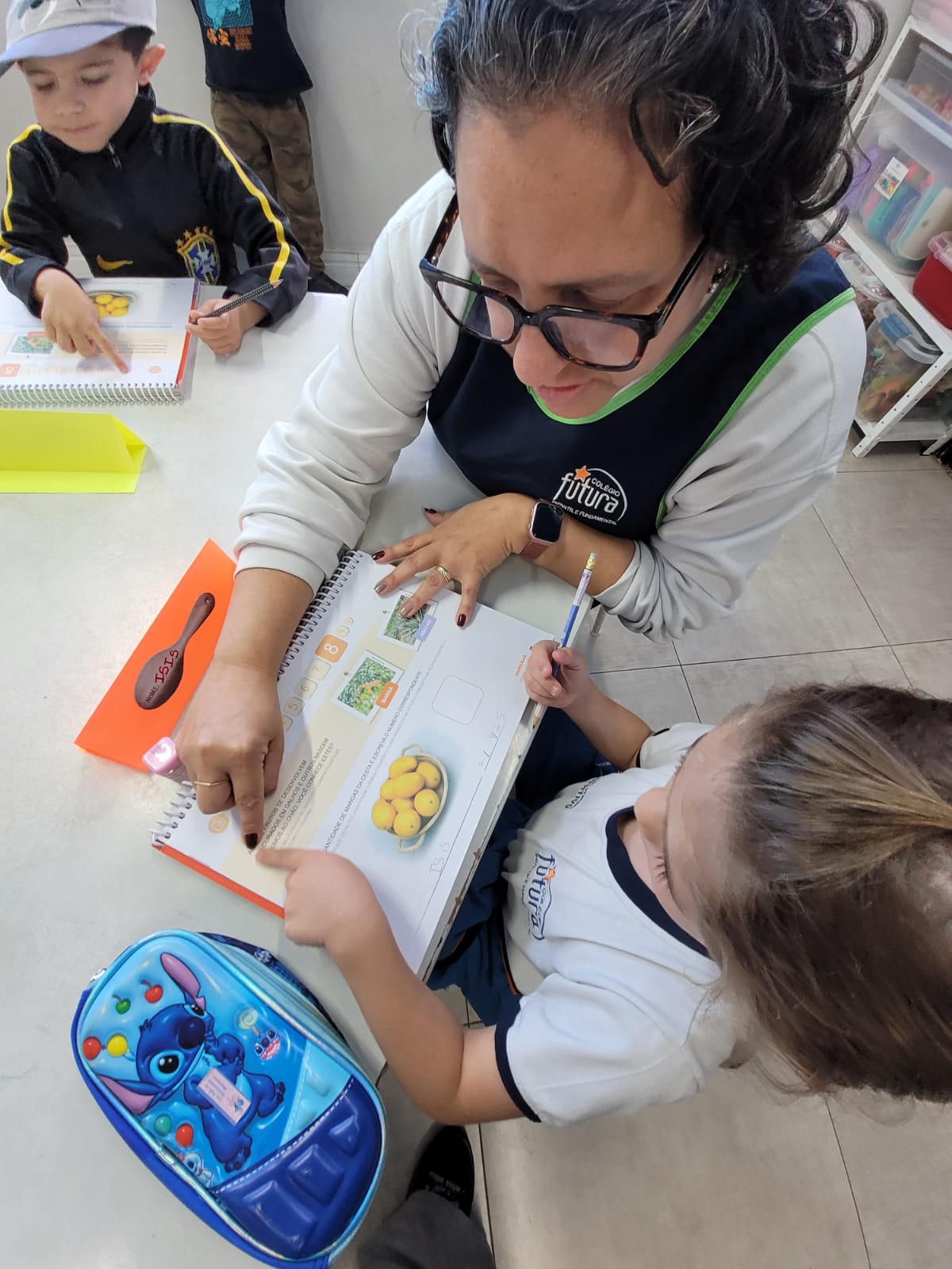Professora do Colégio Futura Infantil em Jundiaí auxiliando aluna em atividade pedagógica, promovendo aprendizado individualizado e atenção às crianças.