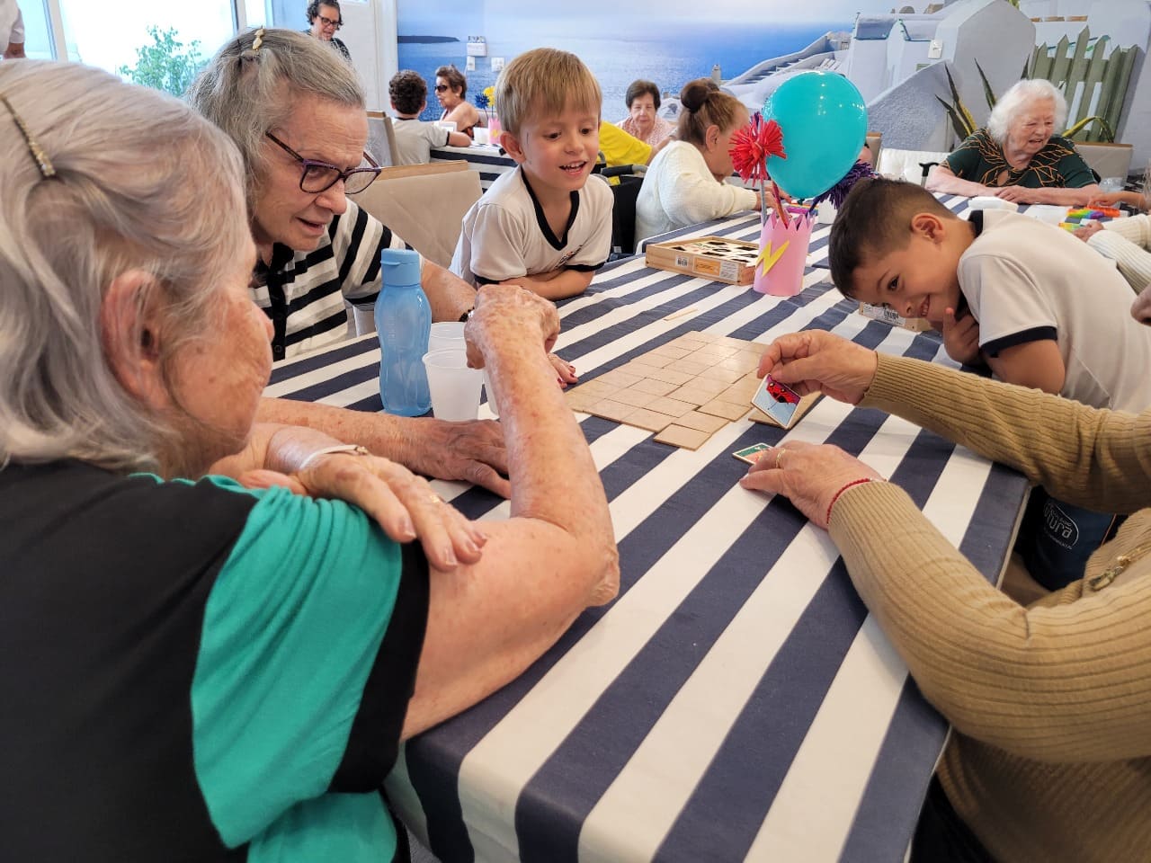 Crianças e idosas sorrindo e jogando jogo de cartas/mesa no Residencial Splendore Jundiaí.