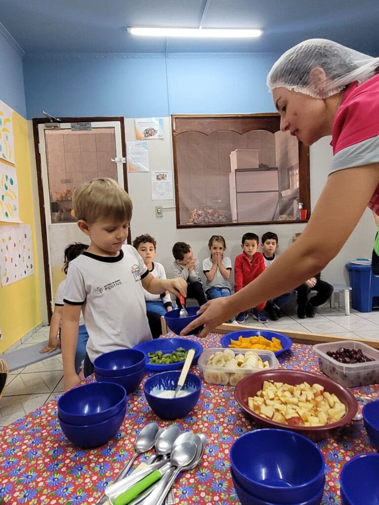 Criança pegando frutas para degustação com a ajuda da nutricionista no Colégio Futura Jundiaí, incentivando protagonismo infantil.