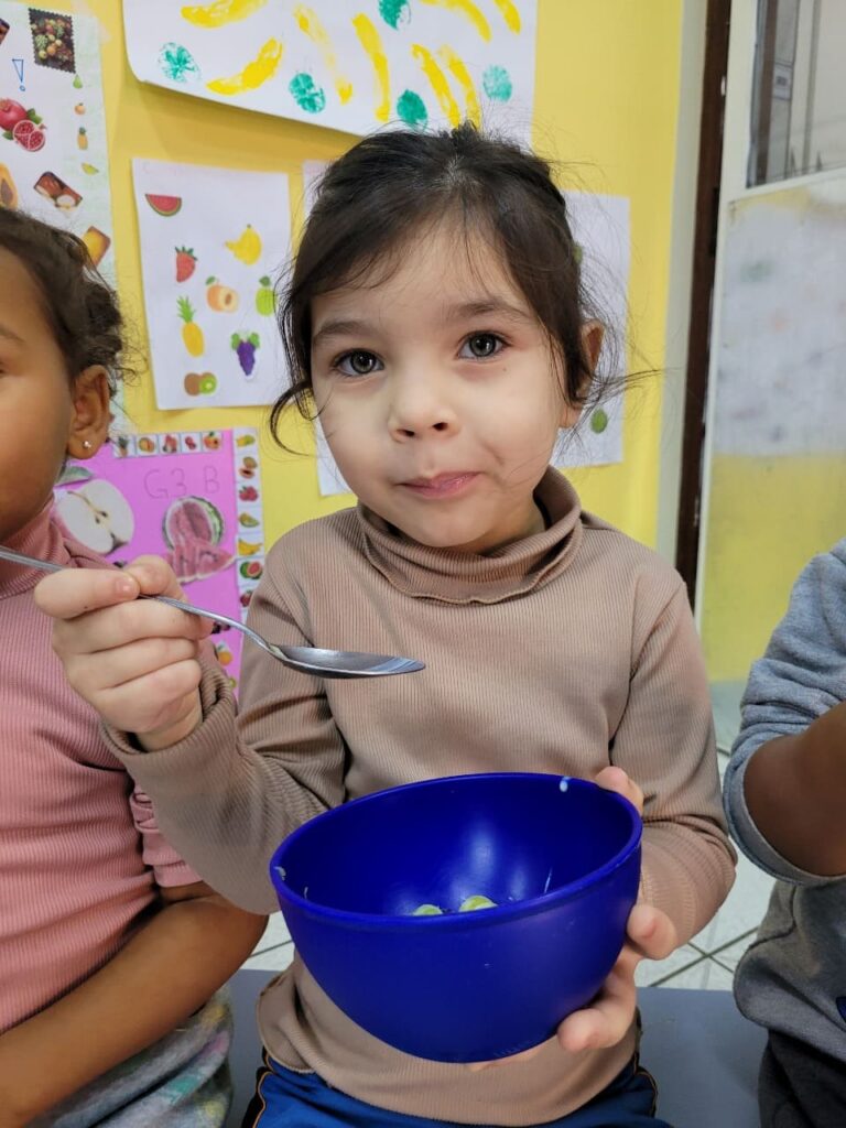 Criança do Colégio Futura Jundiaí comendo salada de frutas em tigela azul durante vivência sobre alimentação saudável.