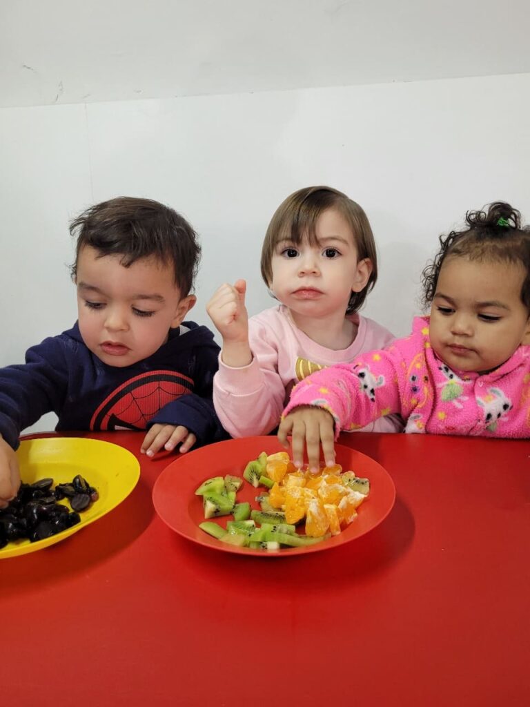 Bebês do Colégio Futura Jundiaí explorando uvas, kiwi e laranja em vivência sensorial com frutas.