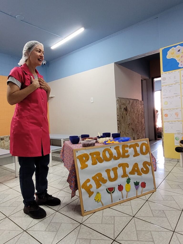 Nutricionista Ana Paula Silva ao lado do painel "Projeto Frutas" na aula de alimentação saudável do Colégio Futura Jundiaí.