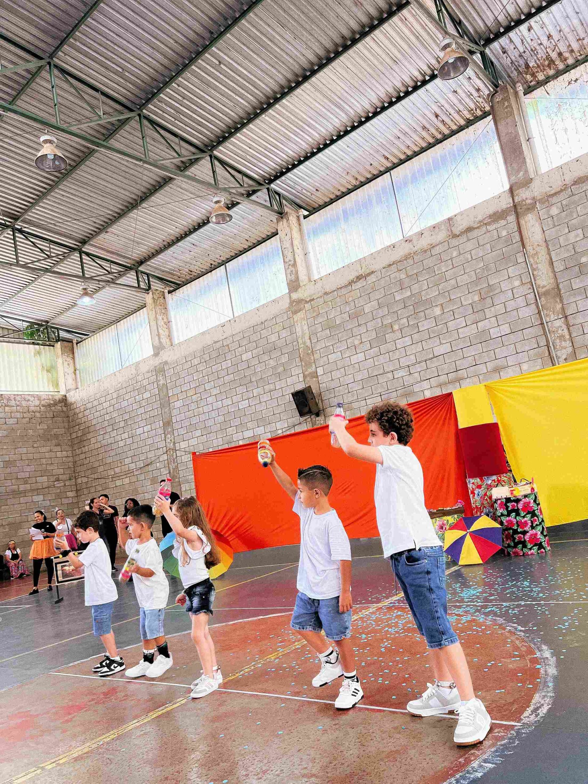 Grupo de crianças em pé, usando maracás reciclados, durante a performance musical do Sarau 2025 no Colégio Futura Infantil Jundiaí.