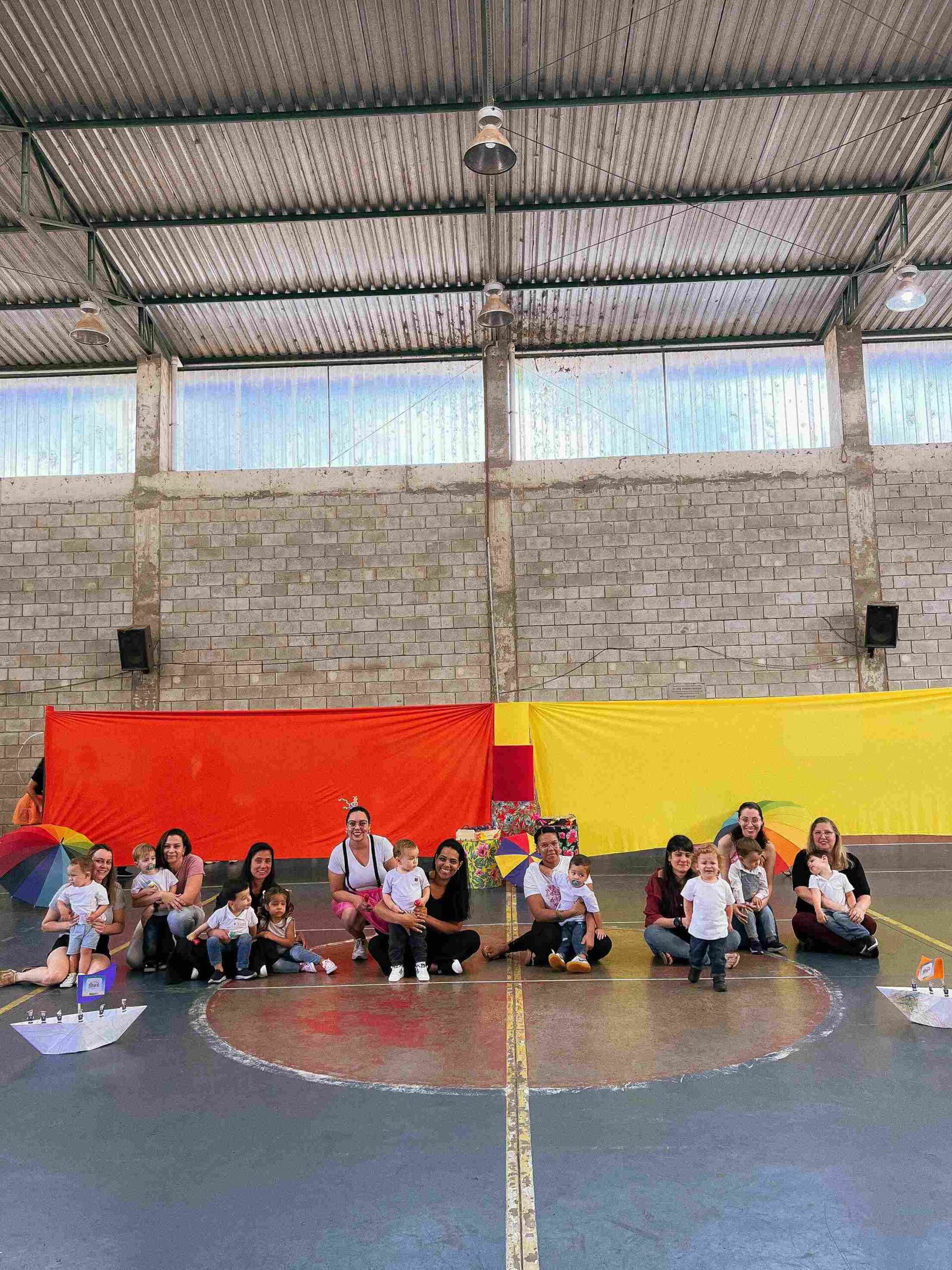 Professoras com bebês da turma do berçário, em frente a barcos de papel, na apresentação do Sarau 2025 do Colégio Futura Jundiaí.