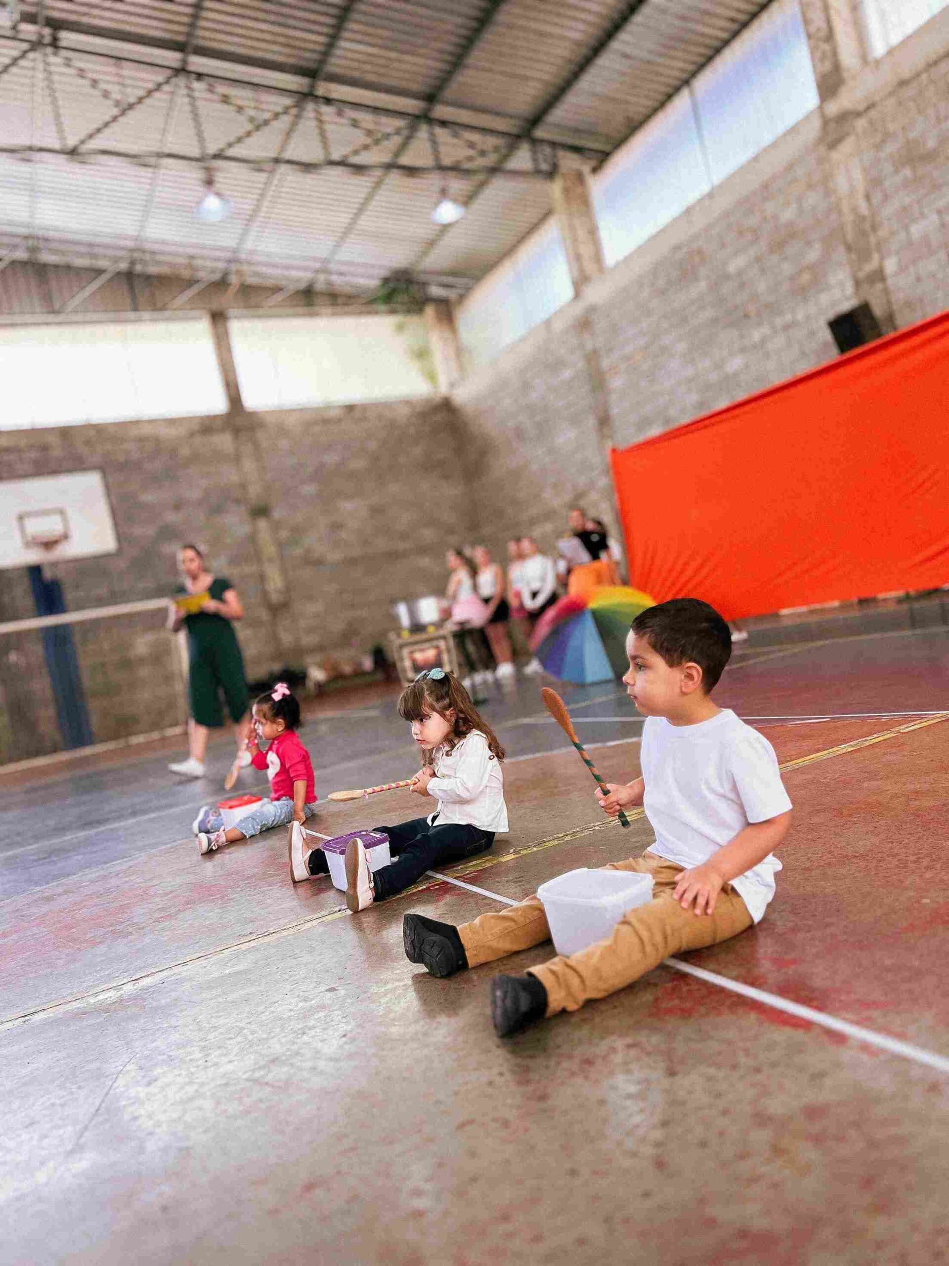 Crianças do Colégio Futura Jundiaí sentadas com potes e colheres grandes em performance de Sarau 2025.