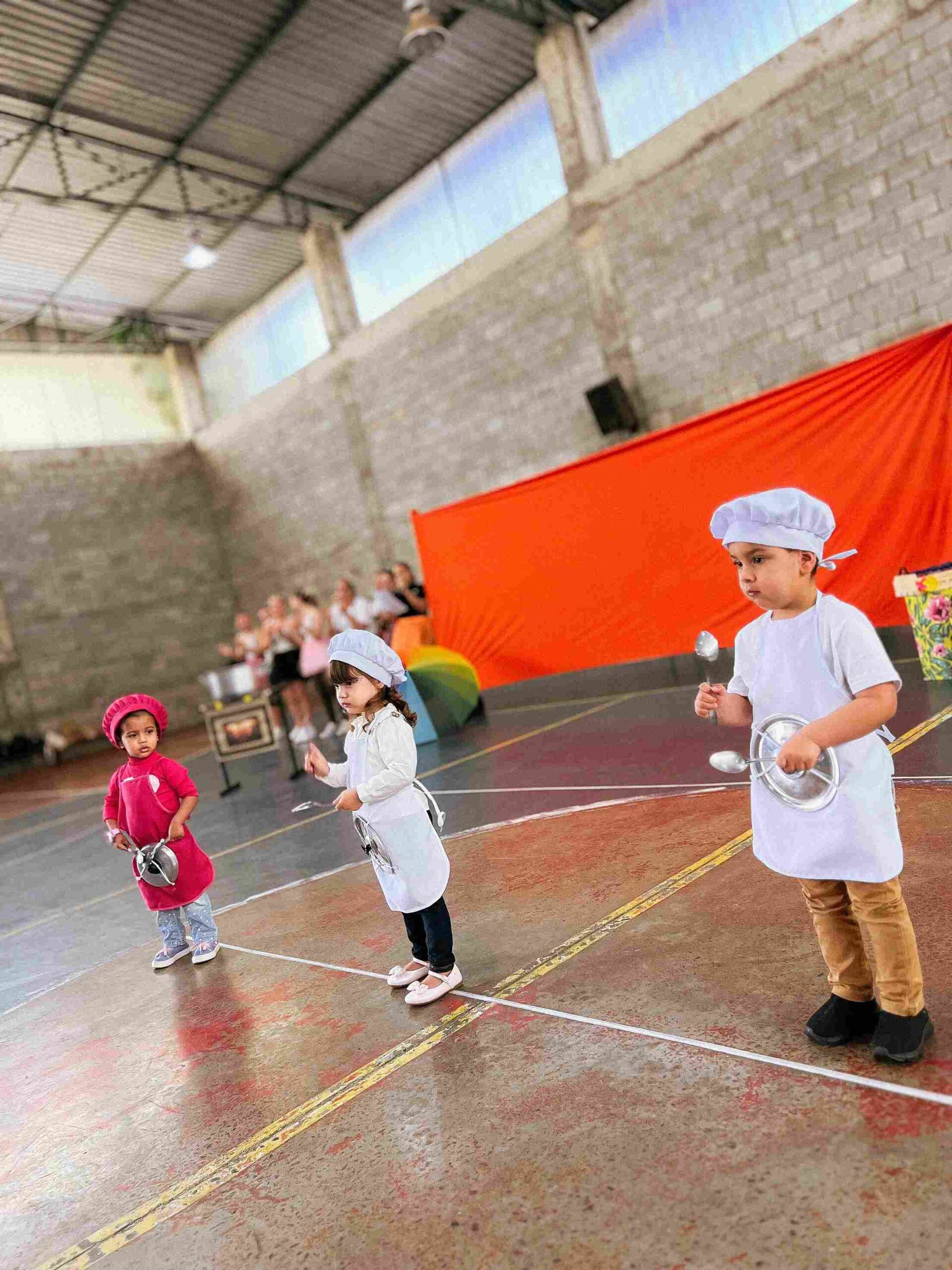 Três crianças vestidas de cozinheiros com panelas durante a coreografia do Sarau 2025 do Colégio Futura Jundiaí.