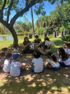 Alunos do Colégio Futura Infantil Jundiaí Grupo 3 sentados em círculo à beira do lago no Jardim Botânico, ouvindo contação de histórias sobre a natureza com educadores.