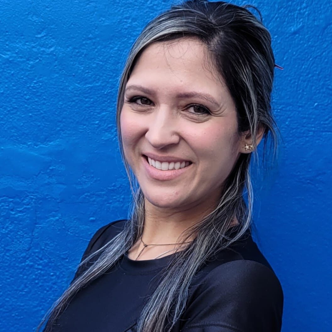 Professora Nathali do Colégio Futura Infantil de Jundiaí, sorrindo, em frente a uma parede azul.